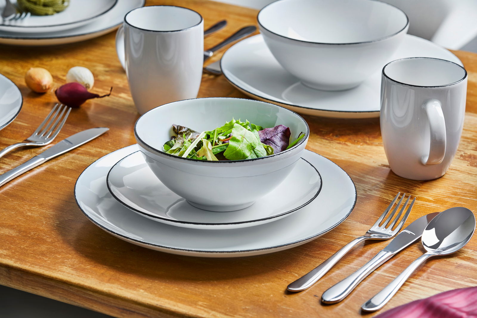 Elegantes Kombiservice 24-teilig Black Star auf einem Holztisch, bestehend aus Tellern, Schalen und Tassen mit schwarzem Rand, aus der Vogelperspektive.