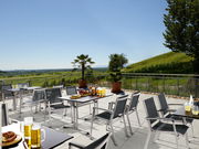 Moderner Gartentisch auf einer Terrasse mit Blick auf eine grüne Landschaft, umgeben von Stühlen und dekoriert mit Getränken und Snacks.