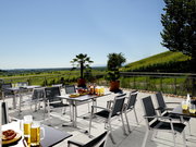 Moderner Gartentisch auf einer Terrasse mit Blick auf eine grüne Landschaft, umgeben von Stühlen und dekoriert mit Getränken und Snacks.