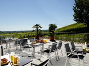 Moderner Gartentisch auf einer Terrasse mit Blick auf eine grüne Landschaft, umgeben von Stühlen und dekoriert mit Getränken und Snacks.