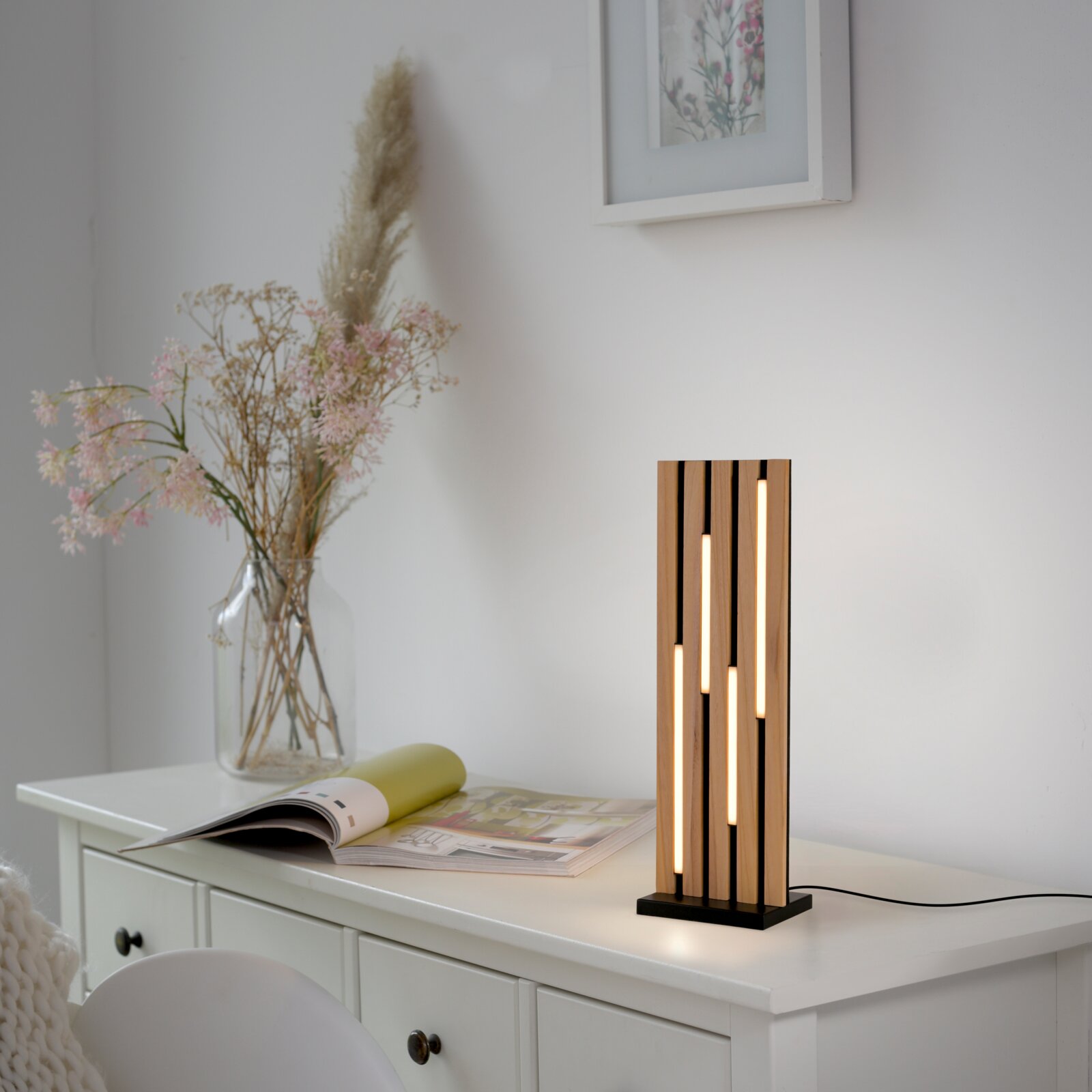 Moderne LED-Tischleuchte mit vertikalen Holzstreifen und warmem Licht, seitliche Perspektive auf einem weißen Tisch platziert.