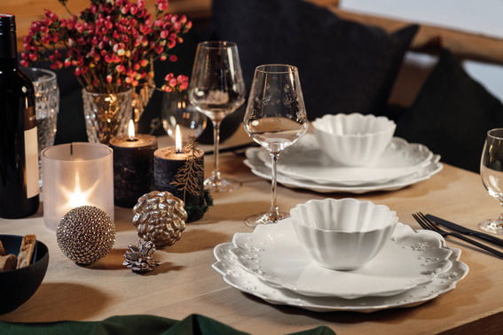 Elegantes Tischarrangement mit Rotweinkelchen im Vordergrund, umgeben von stilvollen Tellern und dekorativen Elementen in einer gemütlichen Atmosphäre.