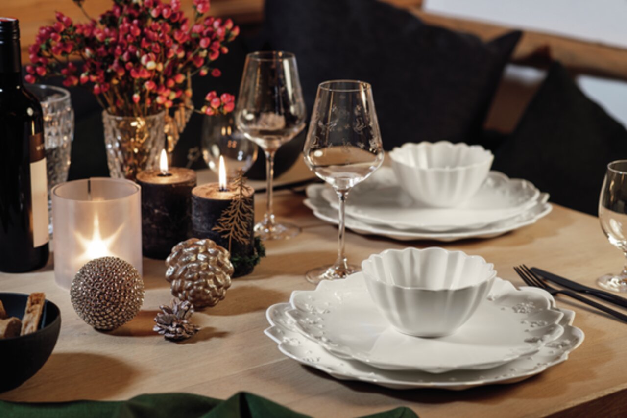 Elegantes Tischarrangement mit Rotweinkelchen im Vordergrund, umgeben von stilvollen Tellern und dekorativen Elementen in einer gemütlichen Atmosphäre.