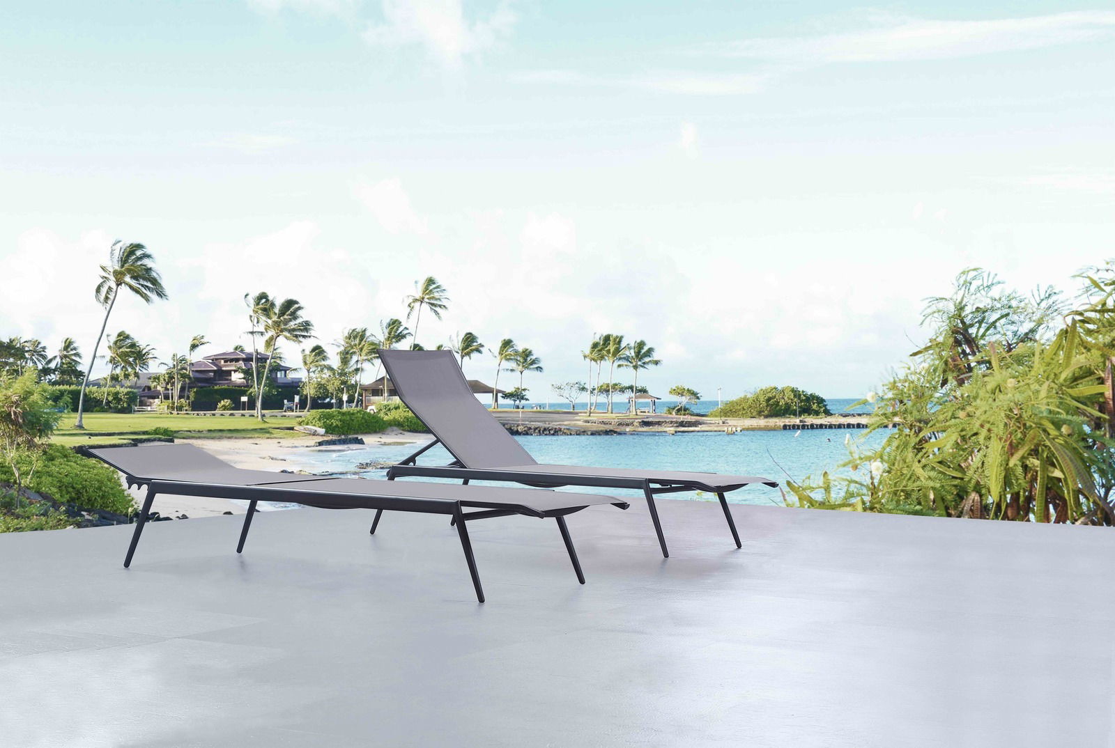 Zwei moderne Sonnenliegen auf einer Terrasse mit Blick auf einen tropischen Strand und Palmen im Hintergrund.