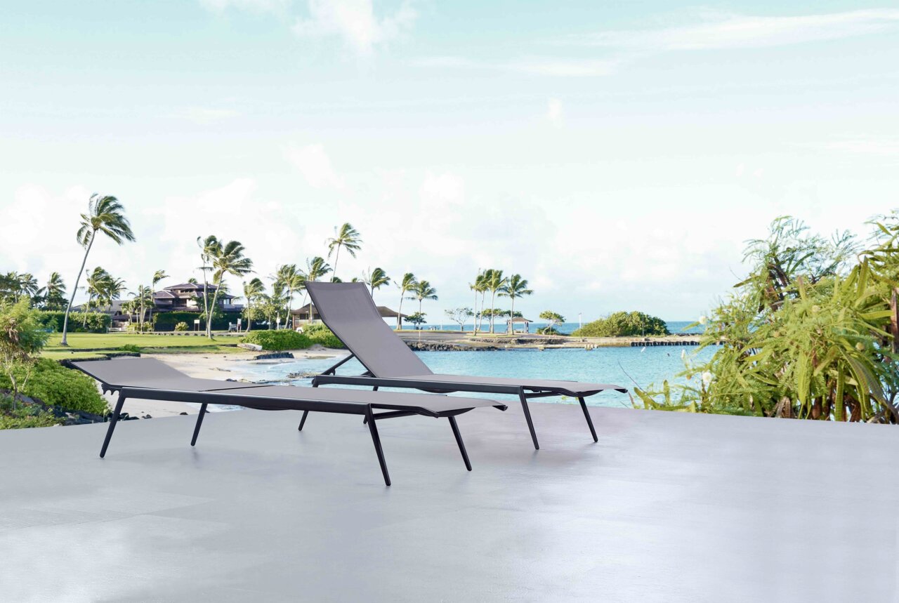 Zwei moderne Sonnenliegen auf einer Terrasse mit Blick auf einen tropischen Strand und Palmen im Hintergrund.