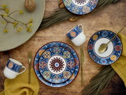 Bunt gemustertes Keramik-Geschirrset mit Tellern, Schälchen und Tassen in Blau-Rot-Orange auf Holztisch, Draufsicht (Flatlay)