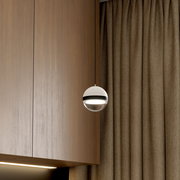 Moderne kugelförmige Pendelleuchte in Weiß mit schwarzem Ring und glänzendem Unterteil, eingeschaltet vor Holzpaneel und beigem Vorhang, seitliche Ansicht