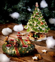 Großer Tannenbaum mit Kindern, dekoriert mit Figuren und Weihnachtsmotiven, auf einem Holztisch mit künstlichem Schnee, seitliche Perspektive.