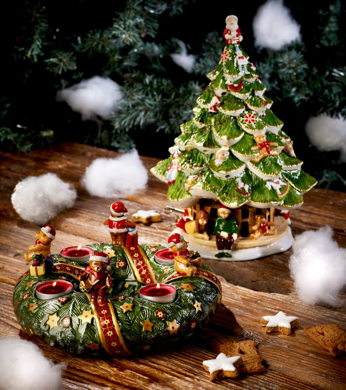 Großer Tannenbaum mit Kindern, dekoriert mit Figuren und Weihnachtsmotiven, auf einem Holztisch mit künstlichem Schnee, seitliche Perspektive.