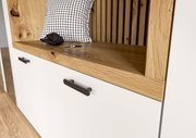 Nahaufnahme einer Kompaktgarderobe mit weißem Schrank, Holzdetails und schwarzen Griffen. Perspektive von schräg oben.