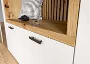 Close-up van een compacte garderobekast met een witte kast, houten details en zwarte handgrepen. Schuin bovenaanzicht.