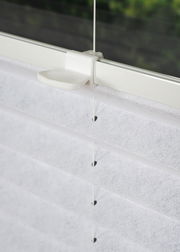 Nahaufnahme eines weißen, gefädelten Plissees an einem Fenster, seitliche Perspektive