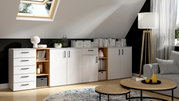 Moderne Wohnzimmermöbel mit weißen Schränken und Regalen, dekoriert mit Büchern und Pflanzen, in einem Raum mit Dachfenster und Stehlampe, seitliche Perspektive.