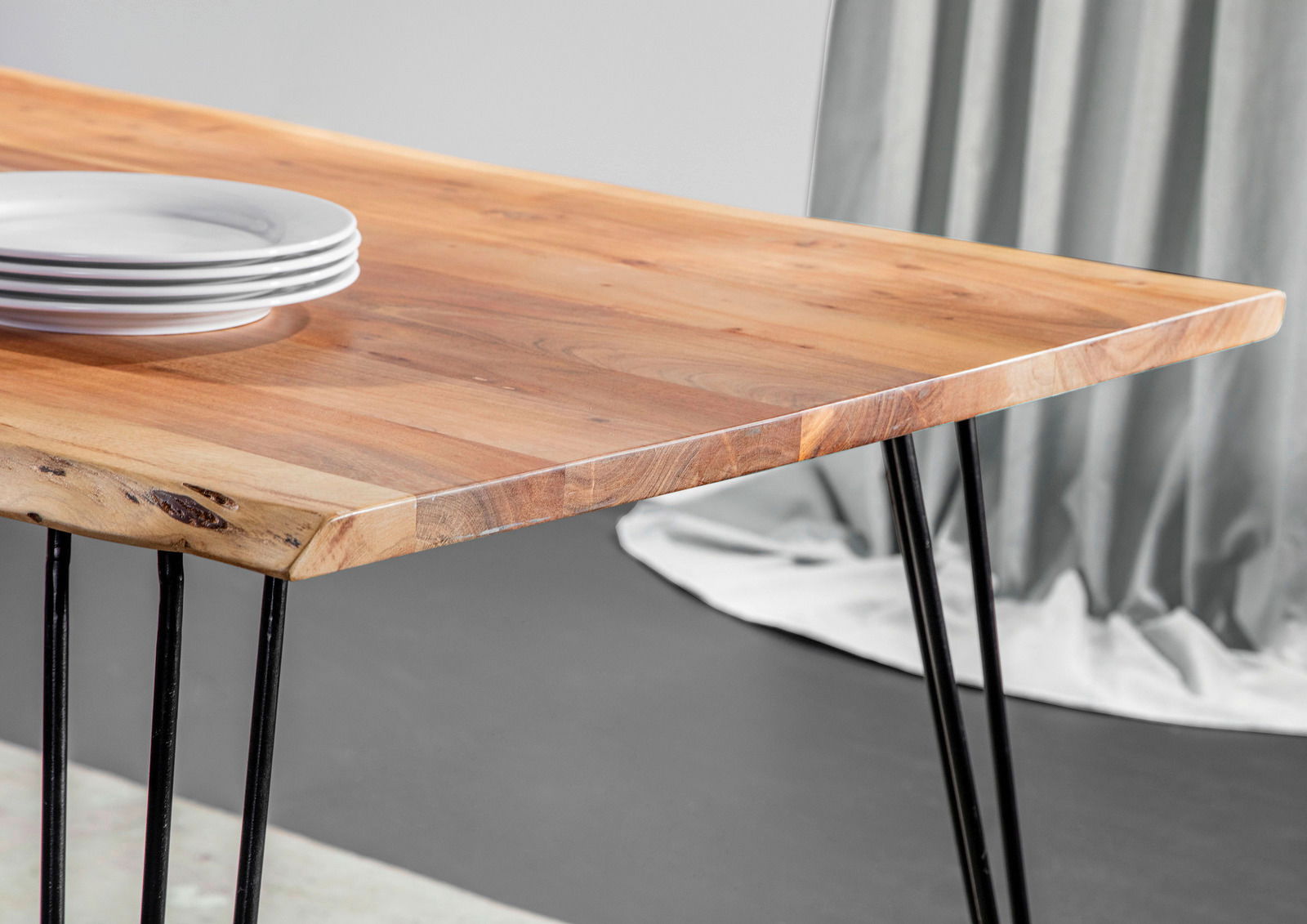 Nahaufnahme eines Esstisches mit Holzplatte und schwarzen Metallbeinen, seitliche Perspektive