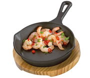 Gusseiserne Grillpfanne mit Garnelen und Chilischoten auf einem Holzbrett, von oben betrachtet.