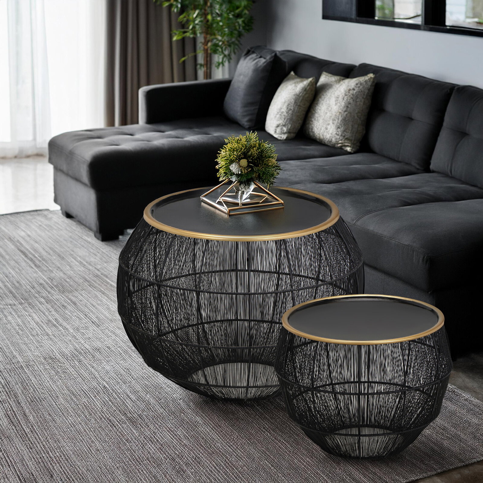 Modernes Beistelltisch 2er-Set mit schwarzem Drahtgestell und runder Tischplatte, im Wohnzimmer neben einem grauen Sofa, aus seitlicher Perspektive.