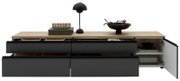 Modernes Sideboard/Lowboard mit schwarzer Front und heller Holzplatte, vier Schubladen und offenem Fach mit rechts geöffneter Tür, dekoriert mit Lampe und Schalen, frontal in leichter Aufsicht auf weißem Hintergrund