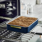 Rechteckige Backform mit blauem Rand und goldenen Griffen, gefüllt mit einem gebackenen Streuselkuchen, auf einem Ofengitter von der Seite fotografiert.
