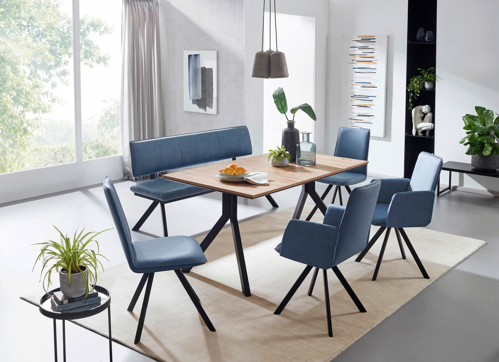 Cantus Esstisch IBIZA Moderner Vierfußtisch aus Holz mit schwarzem Metallgestell, umgeben von blauen Stühlen und einer Bank, in einem hellen Esszimmer mit Pflanzen und Dekorationen. Perspektive: seitlich von oben.