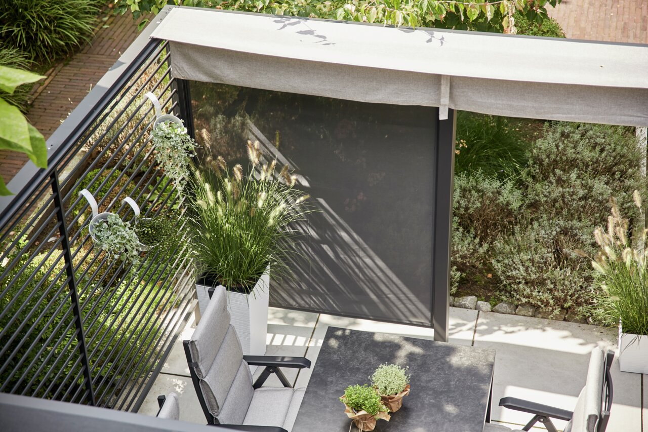 Bovenaanzicht van een terras met een aluminium zichtscherm, omringd door planten en tuinmeubilair.