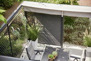 Bovenaanzicht van een terras met een aluminium zichtscherm, omringd door planten en tuinmeubilair.