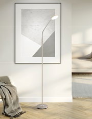 Beige LED-Stehlampe mit schlankem Stab, flexiblem Schwanenhals und rundem Leuchtenkopf auf rundem Standfuß, eingeschaltet, in moderner Wohnzimmerecke vor gerahmtem Wandbild – Frontalansicht
