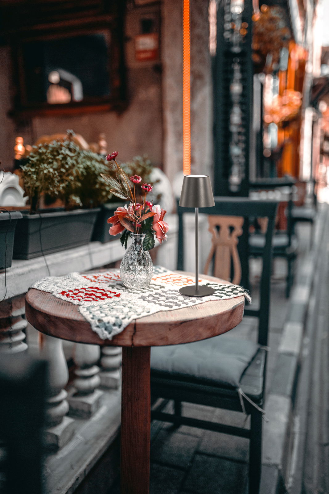 FHL easy Akku-Tischleuchte VILETTO Akku-Tischleuchte VILETTO auf einem runden Holztisch mit gehäkeltem Tischläufer und Blumenvase, seitliche Perspektive.