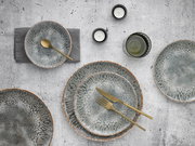 Vogelperspektive auf ein 12-teiliges Tellerset mit organischem Muster in Grau- und Brauntönen, begleitet von goldfarbenem Besteck und Kerzen.