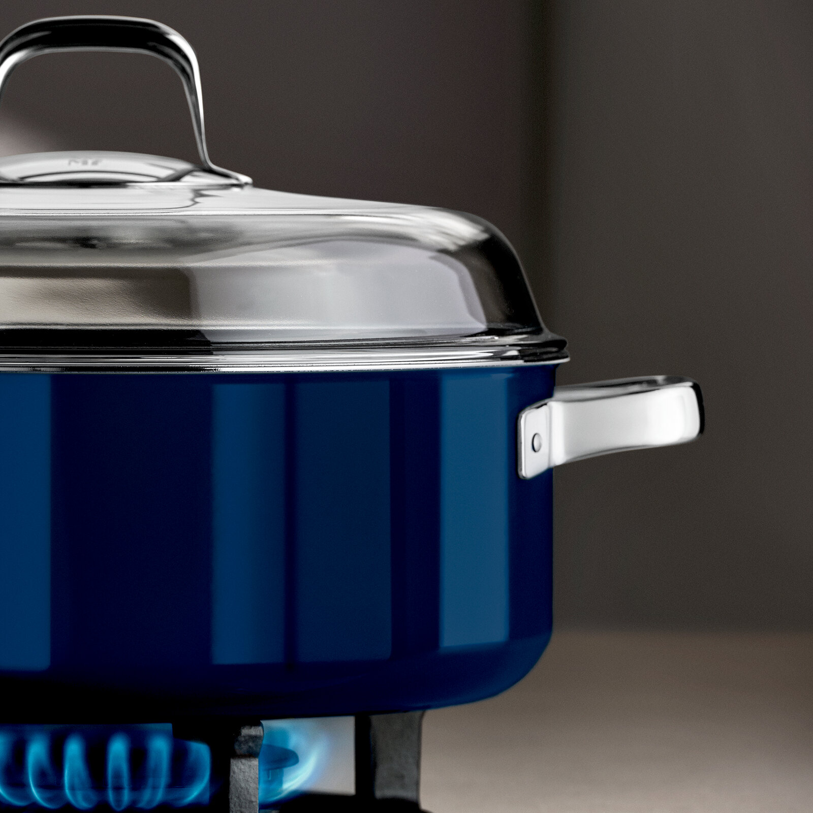 Blauer Schmortopf mit Deckel auf einem Gasherd, seitliche Perspektive