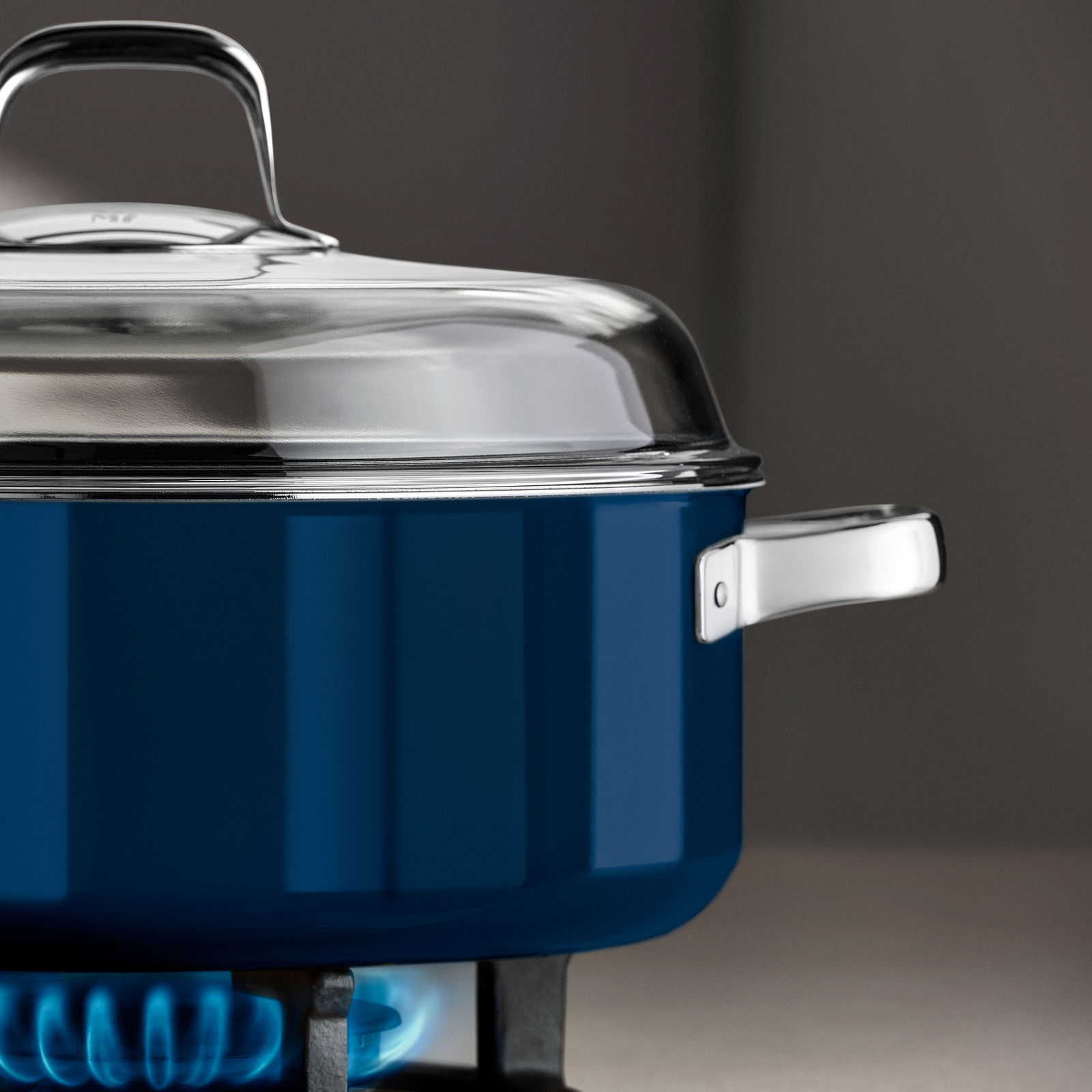 Blauer Schmortopf mit Deckel auf einem Gasherd, seitliche Perspektive