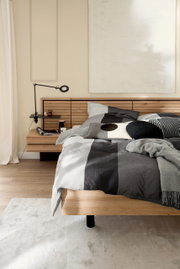 Gemütliches Schlafzimmer mit modernem Holzbett und gestreifter Satin-Bettwäsche in Grau- und Schwarztönen, seitliche Perspektive.