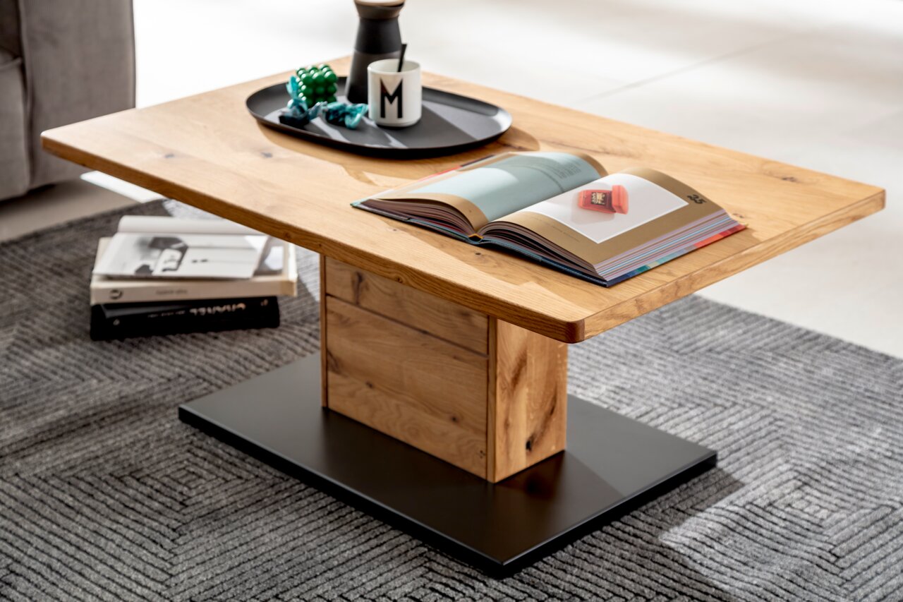 Moderner Couchtisch aus Holz mit rechteckiger Tischplatte, zentralem Standfuß und schwarzer Bodenplatte, seitliche Perspektive.