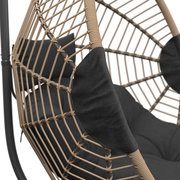 Nahaufnahme eines Hängesessels mit geflochtenem Rattangestell und dunklen Kissen, seitliche Perspektive.