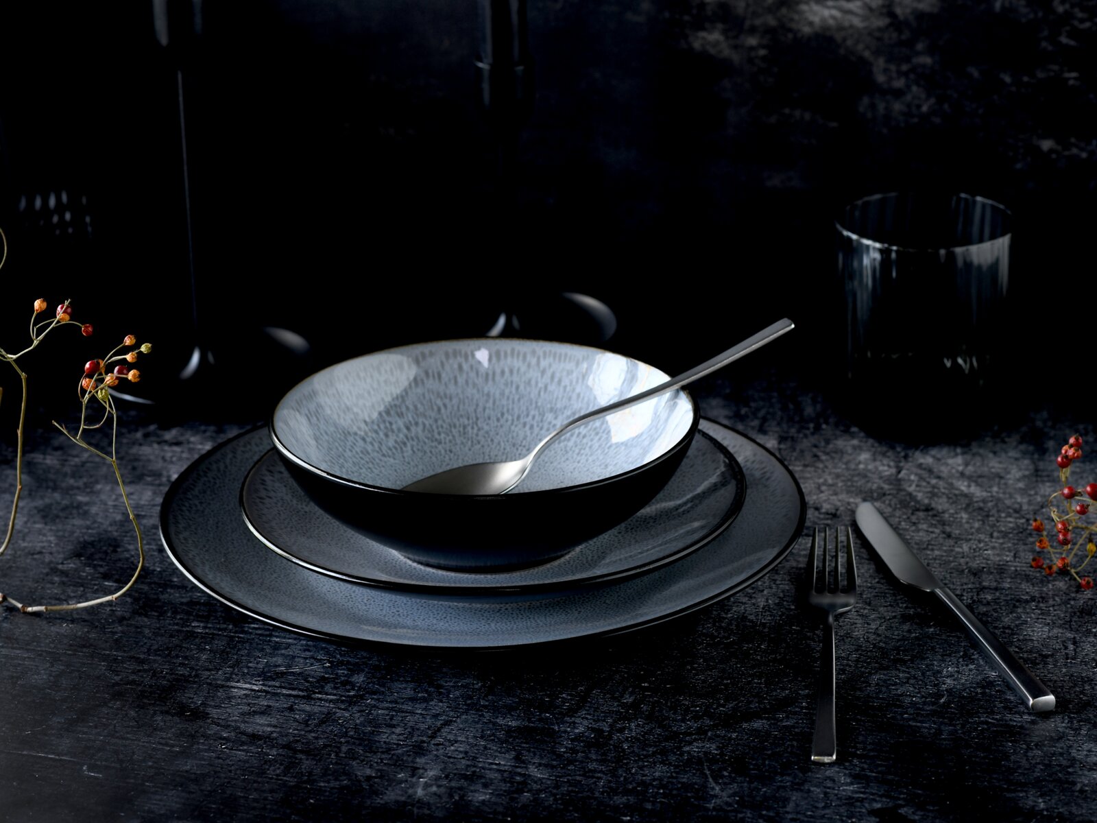 Elegantes Kombiservice 16-tlg in dunklem Design, bestehend aus Schüssel, Teller und Besteck, auf dunklem Hintergrund von schräg oben fotografiert.