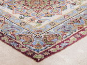 Nahaufnahme eines Orientteppichs mit detailliertem floralen Muster in Rot, Grün, Blau und Beige, von oben fotografiert.