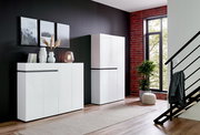 Moderner weißer XXL-Schuhschrank mit vier Türen und einer Schublade, seitliche Perspektive, in einem stilvoll eingerichteten Raum mit dunkler Wand und großen Fenstern.