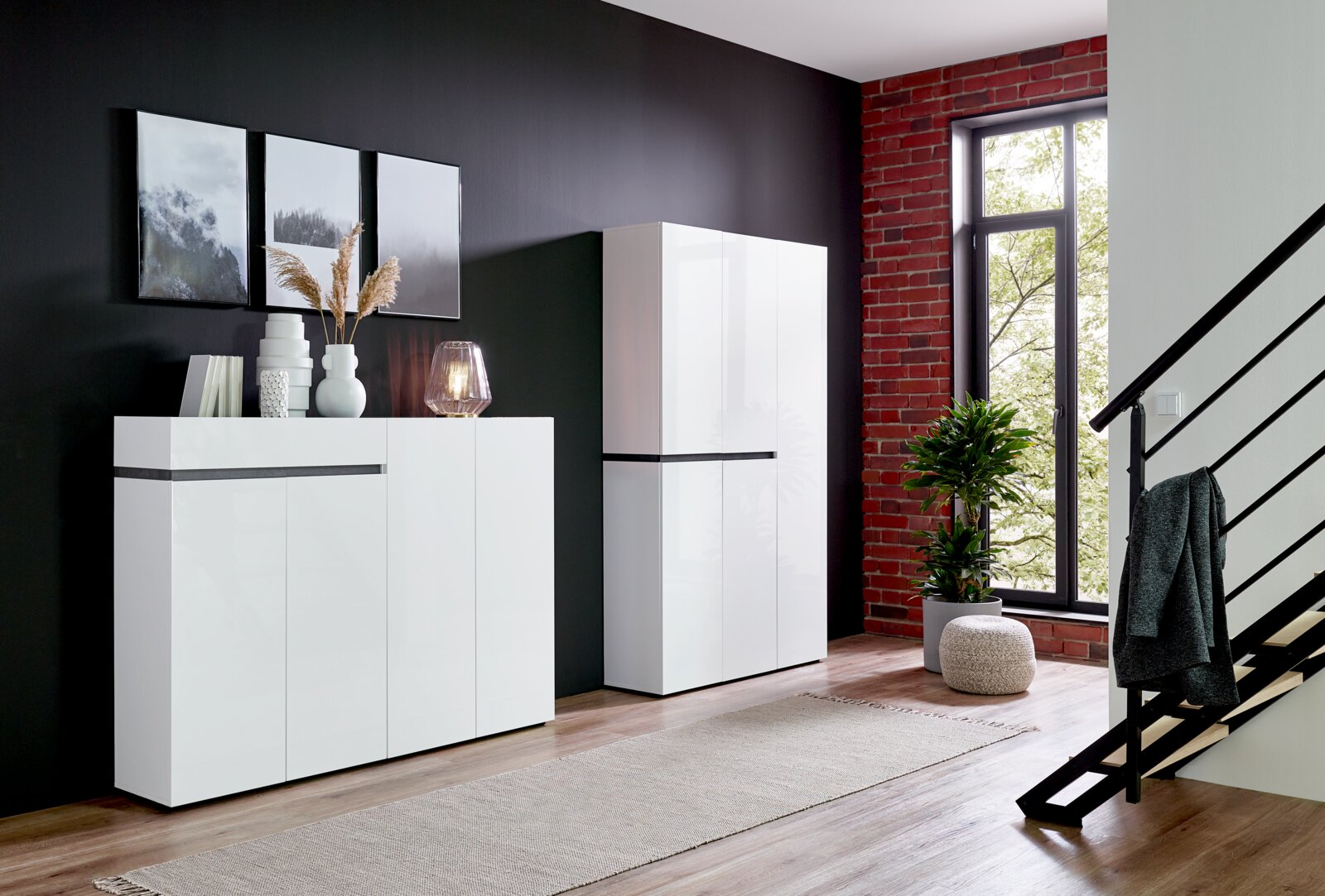 Voleo XXL-schoenenkast YES Moderner weißer XXL-Schuhschrank mit vier Türen und einer Schublade, seitliche Perspektive, in einem stilvoll eingerichteten Raum mit dunkler Wand und großen Fenstern.