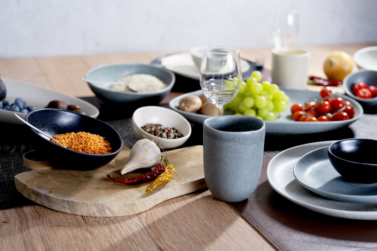 Creatable Speiseteller 4-tlg PIETRA Modernes Keramik-Geschirrset in Blau- und Grautönen auf Holztisch mit Schalen, Tellern und Becher, dekoriert mit Trauben, Tomaten, Linsen, Gewürzen und Glas; Perspektive: leicht seitliche Tischhöhe (3/4-Ansicht)