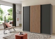 Moderner Schwebetürenschrank mit drei Türen, davon eine mit Holzlamellen, in einem stilvollen Wohnzimmer aus seitlicher Perspektive.