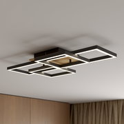Moderne LED-Deckenleuchte mit drei überlappenden, rechteckigen Licht-Rahmen in Schwarz mit Holz-Detail, warmweiß leuchtend, in schräger Untersicht an der Zimmerdecke montiert