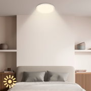 Ronde witte plafondlamp met warm licht in een moderne slaapkamer, vanuit een schuin vooraanzicht van onderen bekeken.