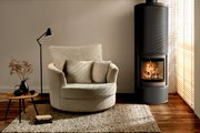 Gemütlicher cremefarbener Sessel mit Kissen, von vorne gesehen, neben einem modernen Kamin in einem stilvoll eingerichteten Wohnzimmer.