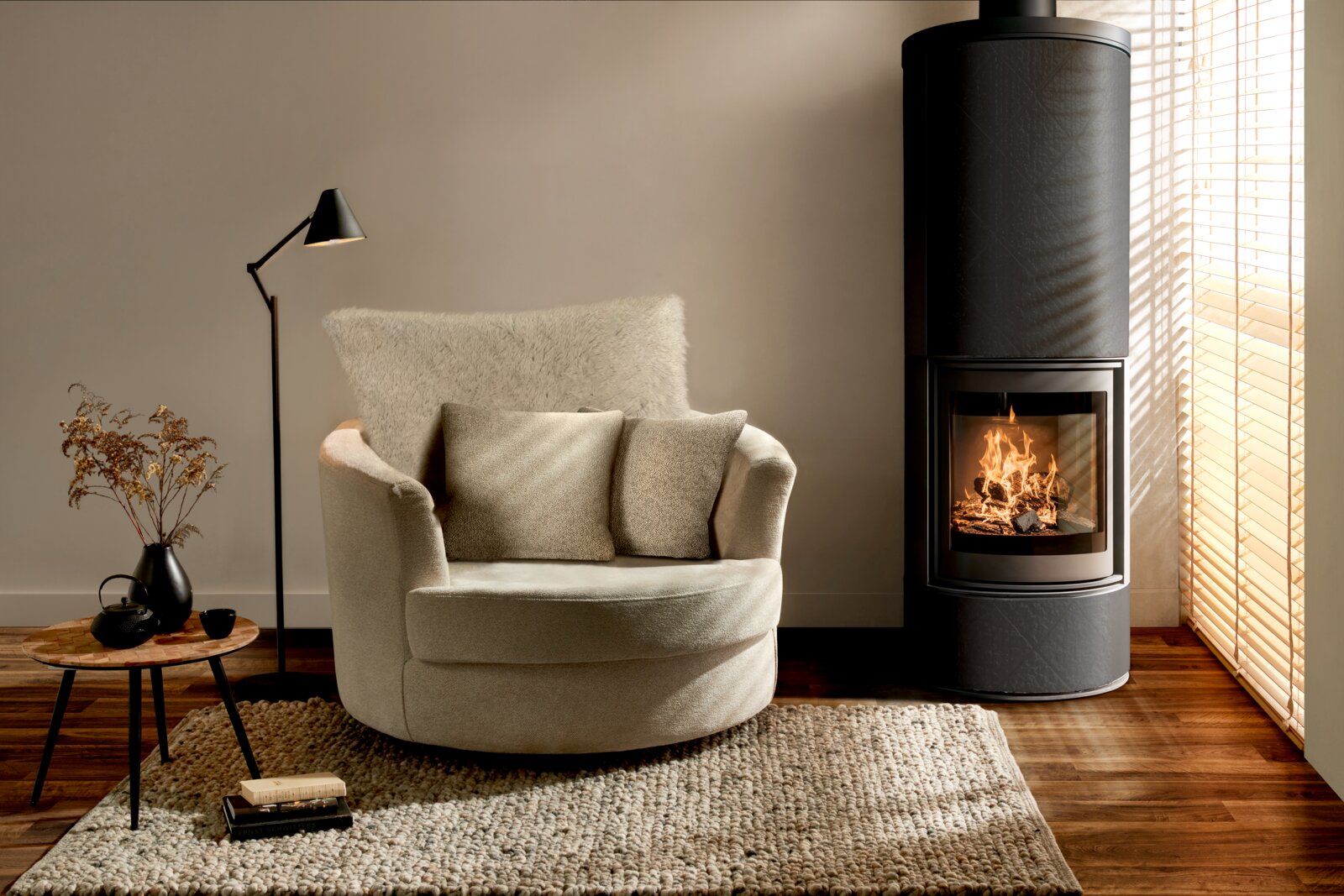 Z2 Fauteuil LENI Een gezellige crèmekleurige fauteuil met kussens, gezien vanaf de voorkant, naast een moderne open haard in een stijlvol ingerichte woonkamer.