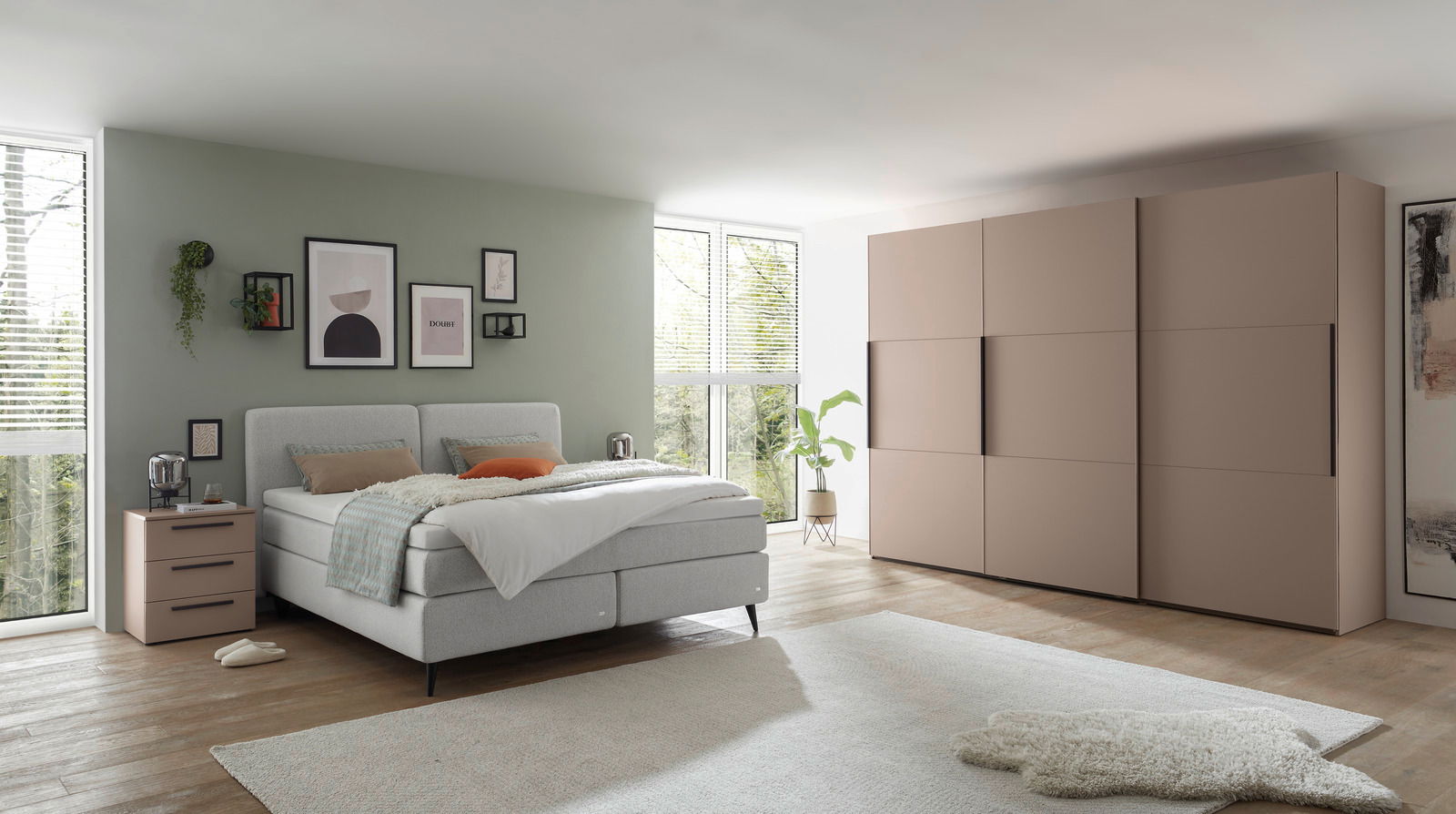 Modernes Boxspringbett in einem stilvoll eingerichteten Schlafzimmer mit grüner Wand, dekorativen Bildern und einem großen Kleiderschrank. Perspektive von der Seite.