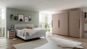 Modernes Boxspringbett in einem stilvoll eingerichteten Schlafzimmer mit grüner Wand, dekorativen Bildern und einem großen Kleiderschrank. Perspektive von der Seite.