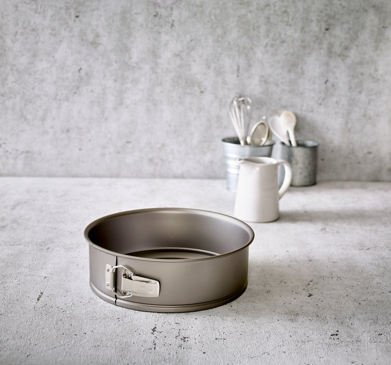 Birkmann Springform Ø26,5cm BASIC BAKING Springform mit einem Durchmesser von 26 cm, auf einer Küchenarbeitsplatte platziert, mit Küchenutensilien im Hintergrund.