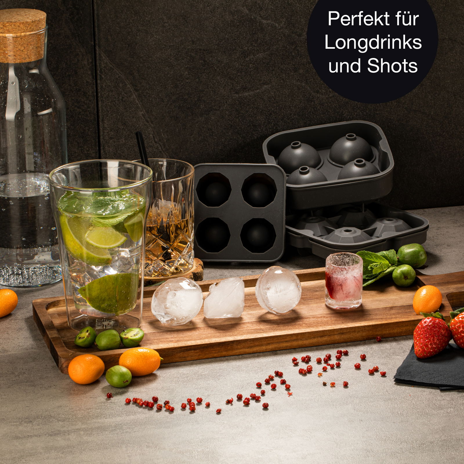 Runde Eiswürfelform mit fertigen Eiskugeln auf einem Holztablett, umgeben von Getränken und Früchten, aus der Perspektive von vorne.