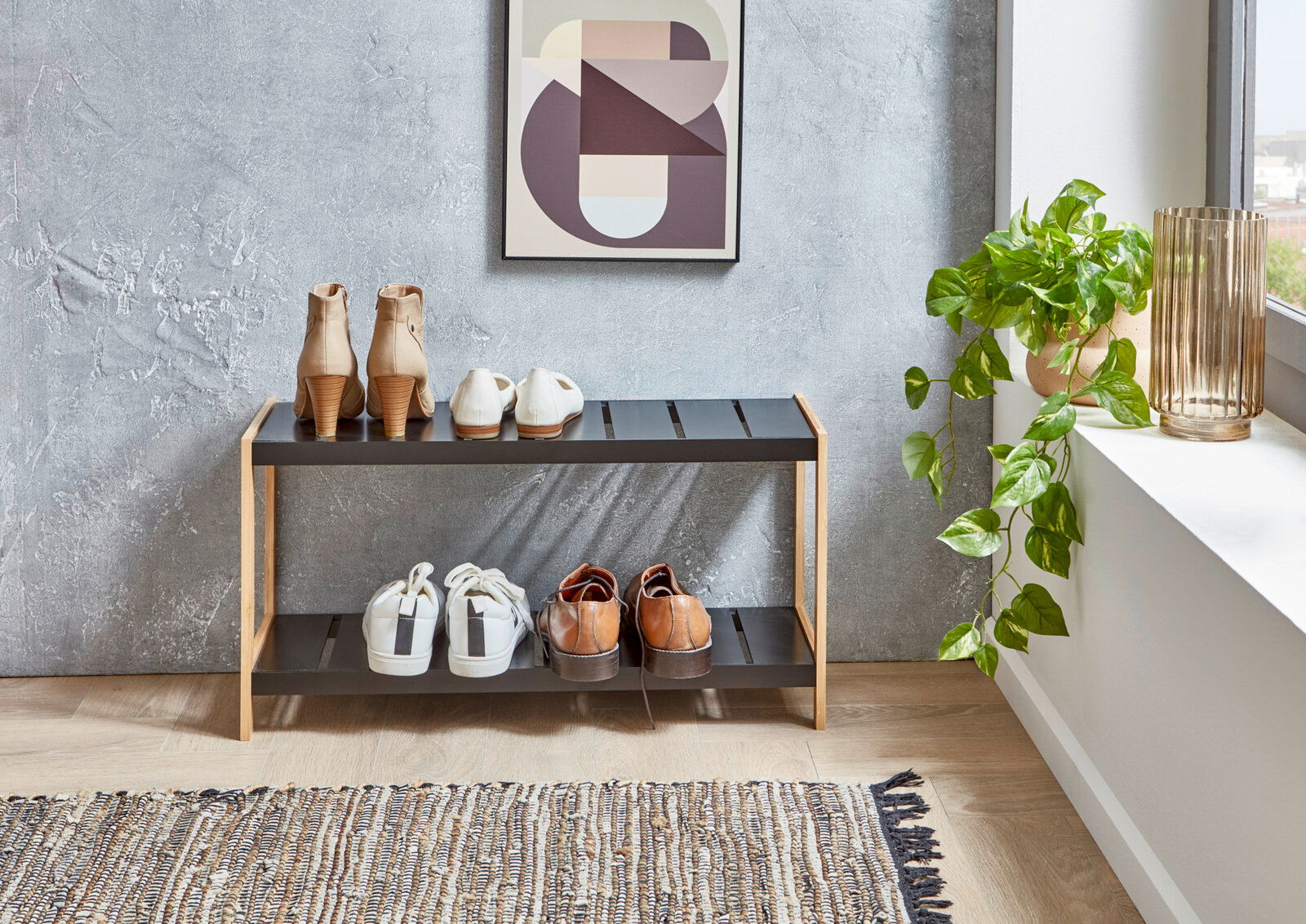 Modernes Schuhregal mit zwei Ebenen, schwarzer Ablage und Holzrahmen, mit mehreren Paar Schuhen bestückt; Frontalansicht im Eingangsbereich neben Fenster und Zimmerpflanze.