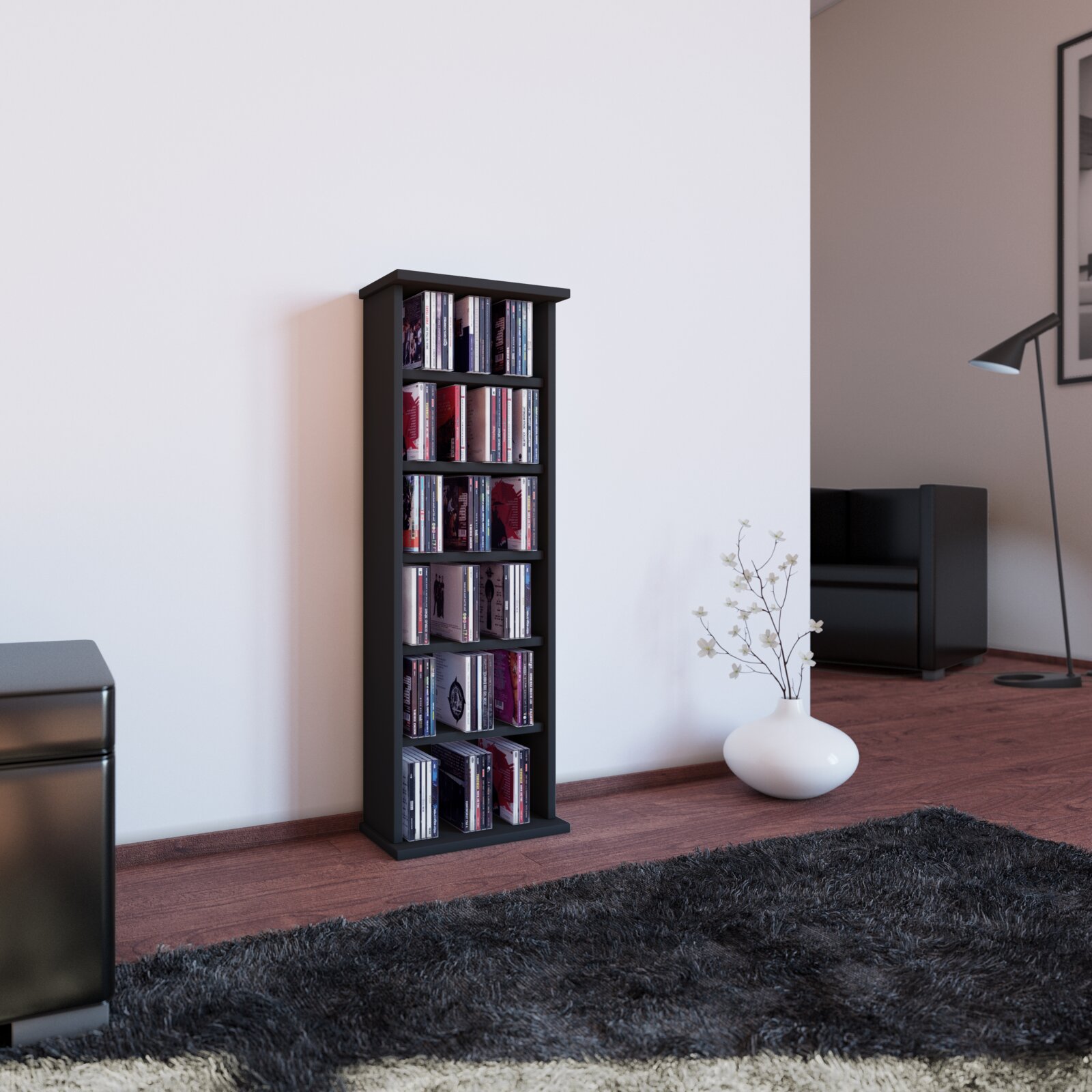 Schmales, schwarzes CD-/DVD-Regal mit mehreren Fächern, gefüllt mit Medienhüllen, freistehend im Wohnzimmer vor weißer Wand Perspektive: frontale Ansicht auf Augenhöhe, leicht von links.