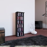 Schmales, schwarzes CD-/DVD-Regal mit mehreren Fächern, gefüllt mit Medienhüllen, freistehend im Wohnzimmer vor weißer Wand; Perspektive: frontale Ansicht auf Augenhöhe, leicht von links.